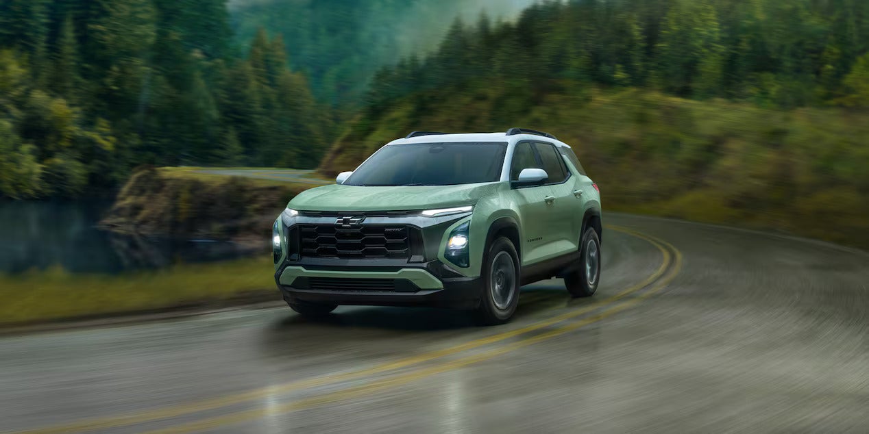 a green suv driving on a paved road in the rain