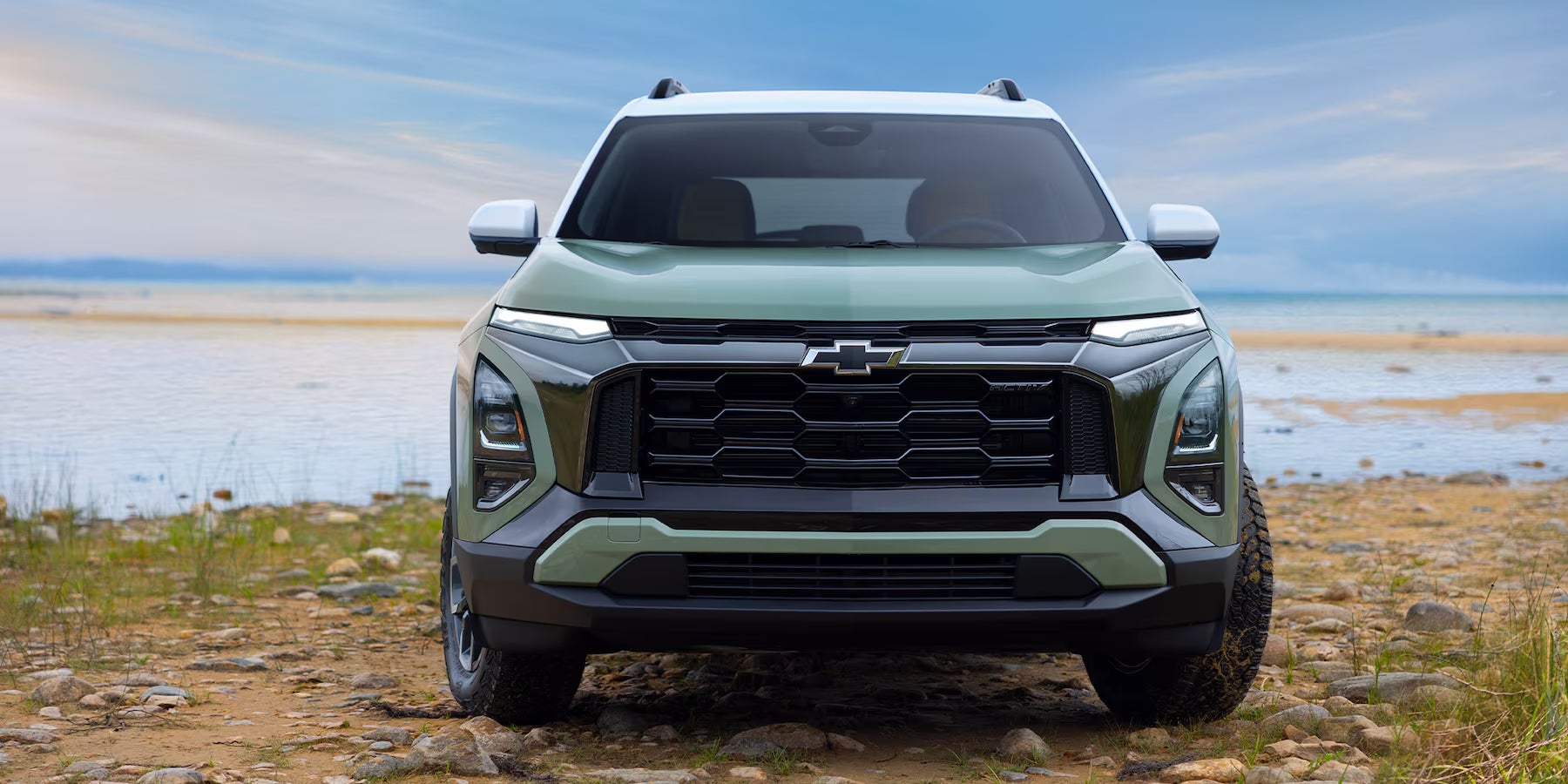 Front end of the light forest green 2025 Chevy Equinox sitting on a beach.