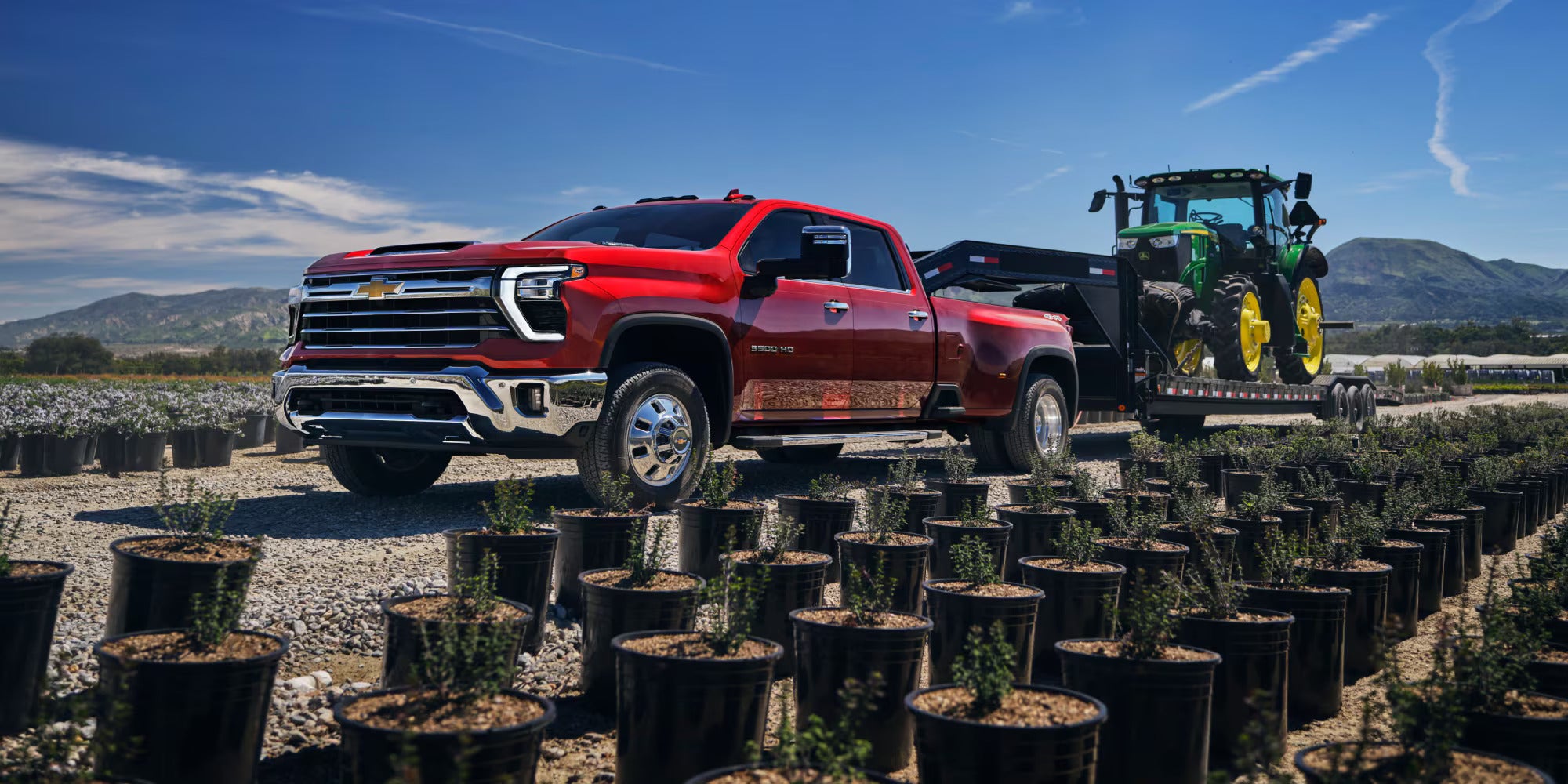 a red truck hauling a john deer tractor next to plants