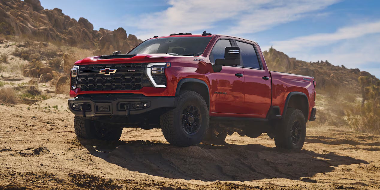 a red silverado 2500 hd parked on dirt with a desert rocky background