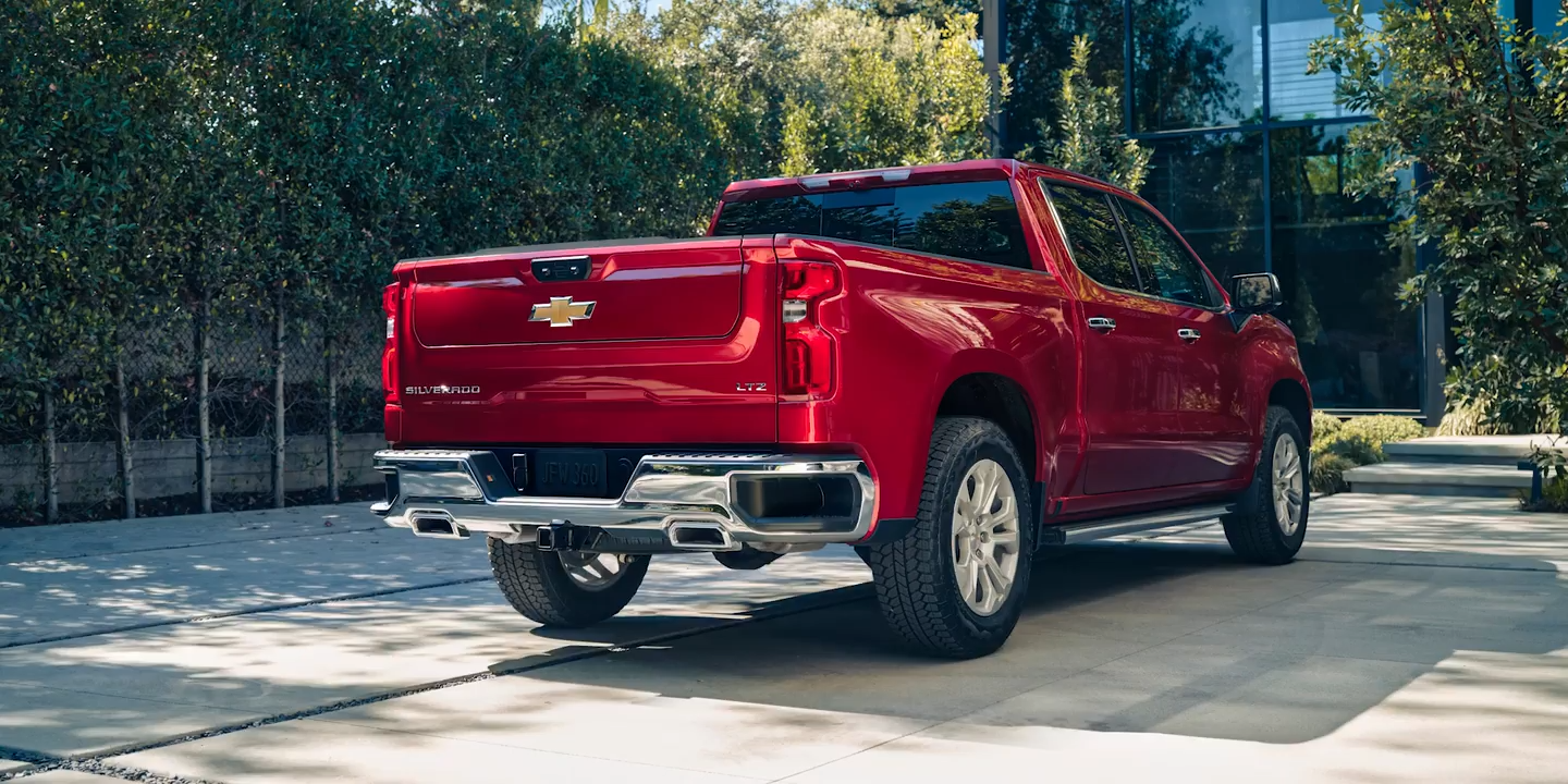 Rear view of a red 2025 Chevrolet Silverado LTZ, parked in a modern driveway, showcasing its stylish tailgate and chrome accents.