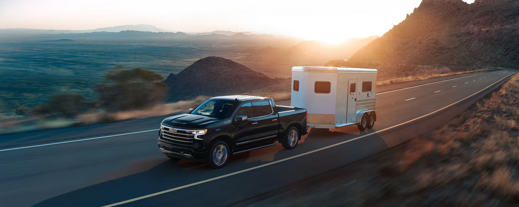 2025 Chevrolet Silverado towing a large trailer on an open road at sunset, highlighting the truck’s towing capabilities.